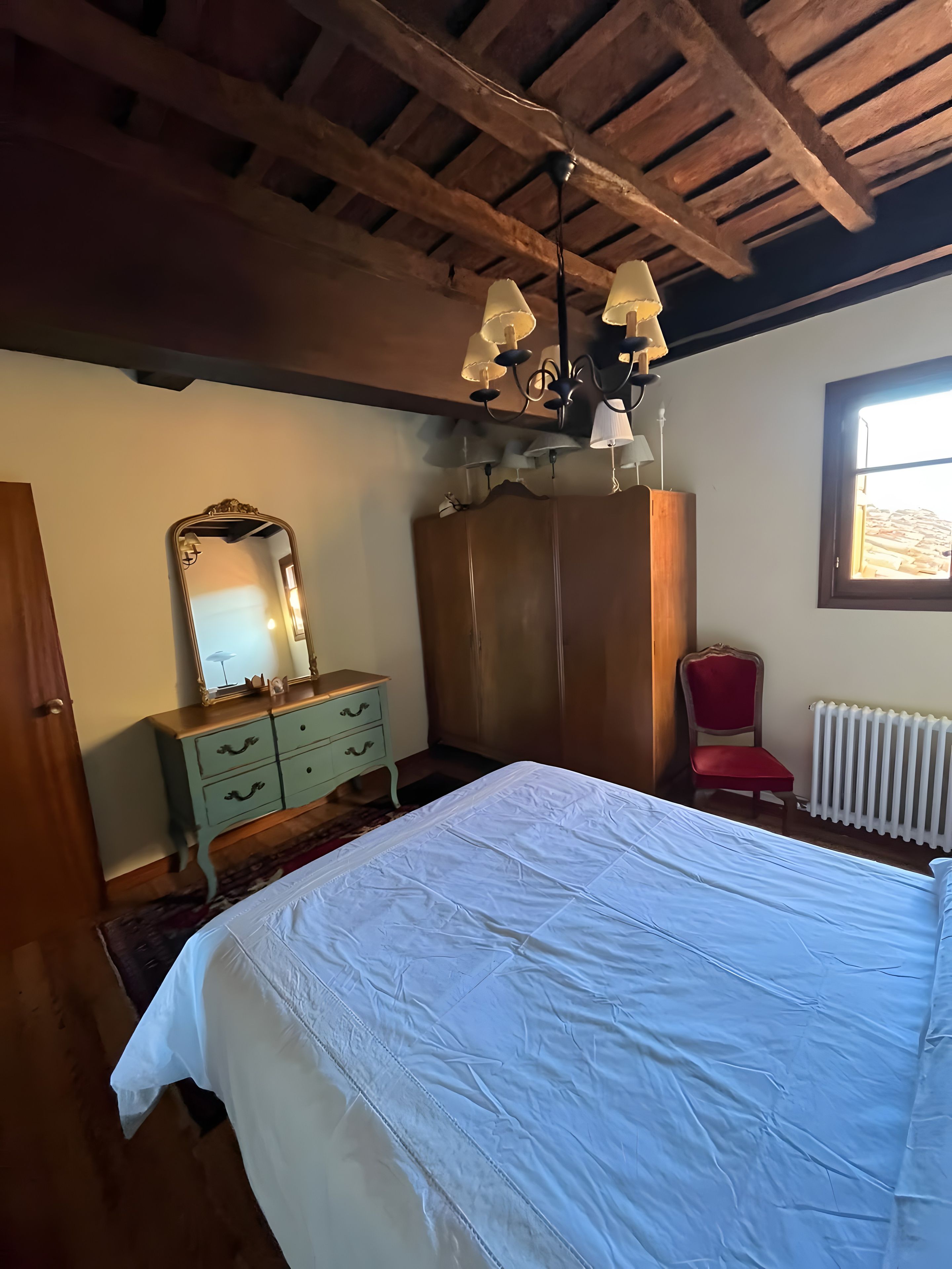 Un dormitorio con una cama grande, un aparador, un espejo, una silla roja y una ventana.