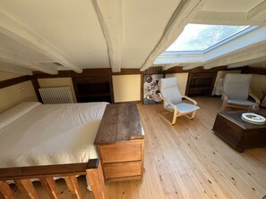 Een slaapkamer met een houten bed, een nachtkastje van hout, een stoel en een kleine tafel. Er is een dakraam boven het bed.