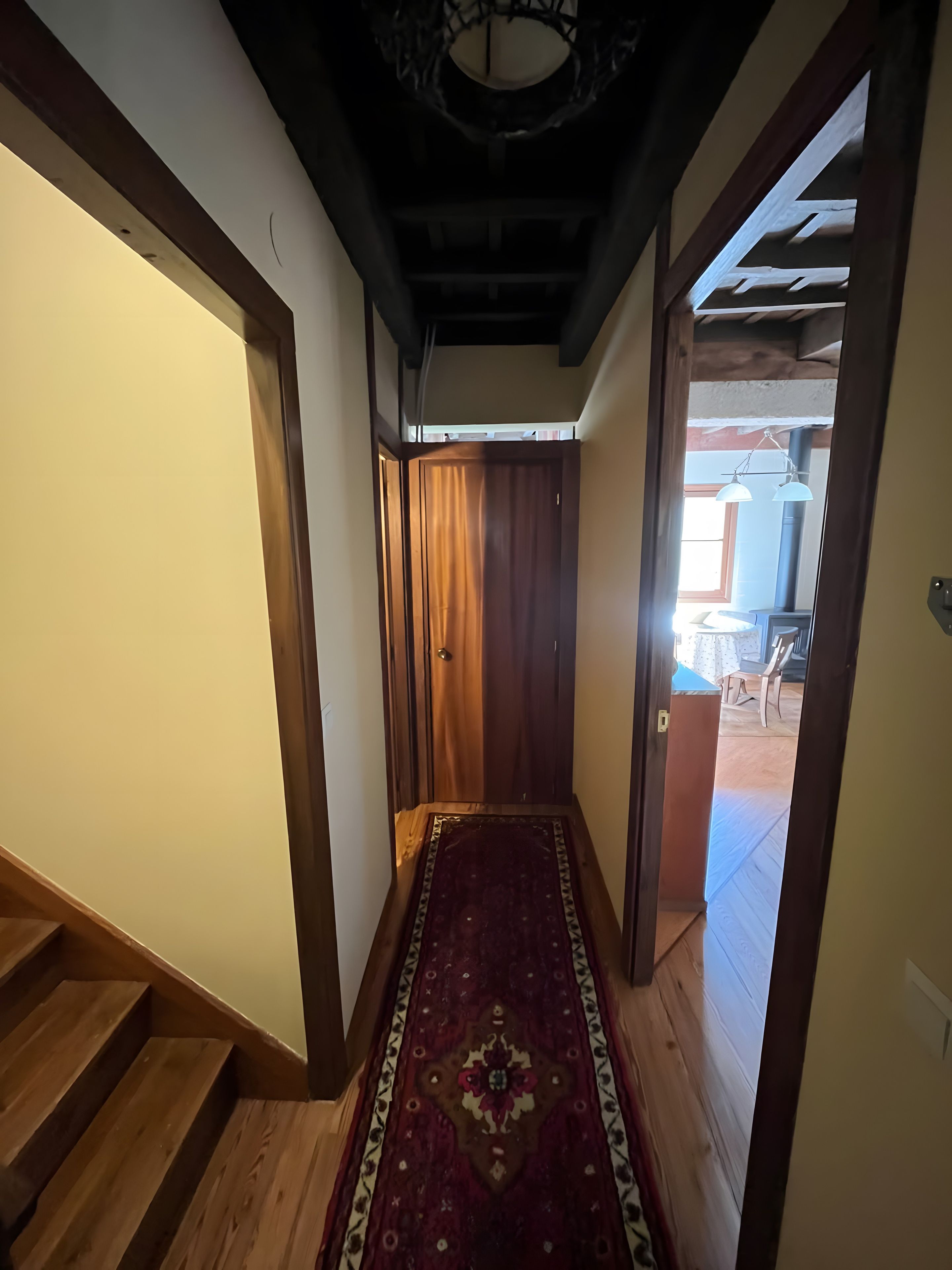 Un pasillo con piso de madera, alfombra estampada y una puerta que da a otra habitación.