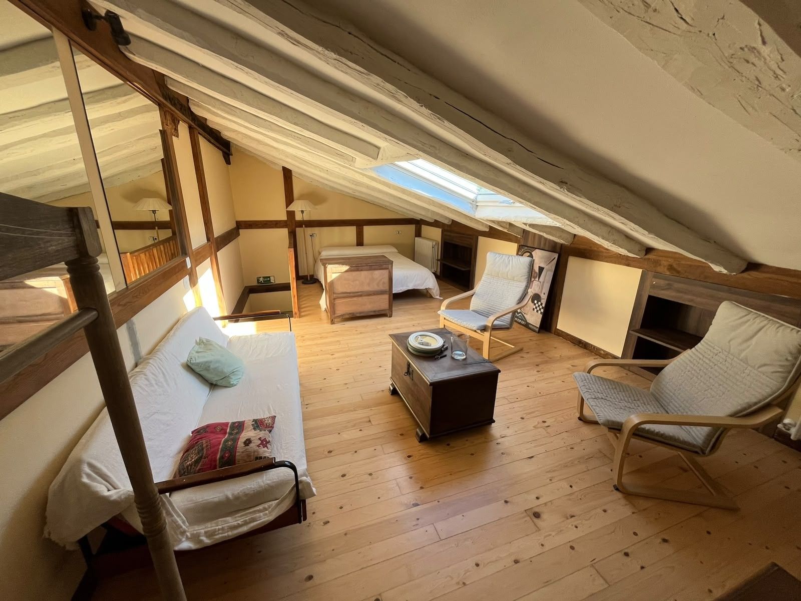 A cozy attic bedroom with a sloped ceiling, wooden beams, a bunk bed, a desk, and a chair.