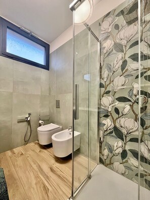 Un baño moderno con cabina de ducha de vidrio, un bidé y un inodoro.