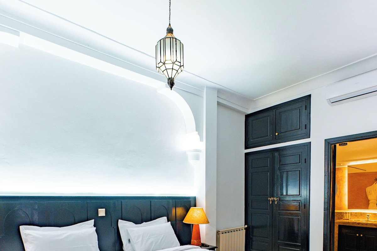 A large bed with white linens, a hanging light fixture, and a dark wooden wardrobe.