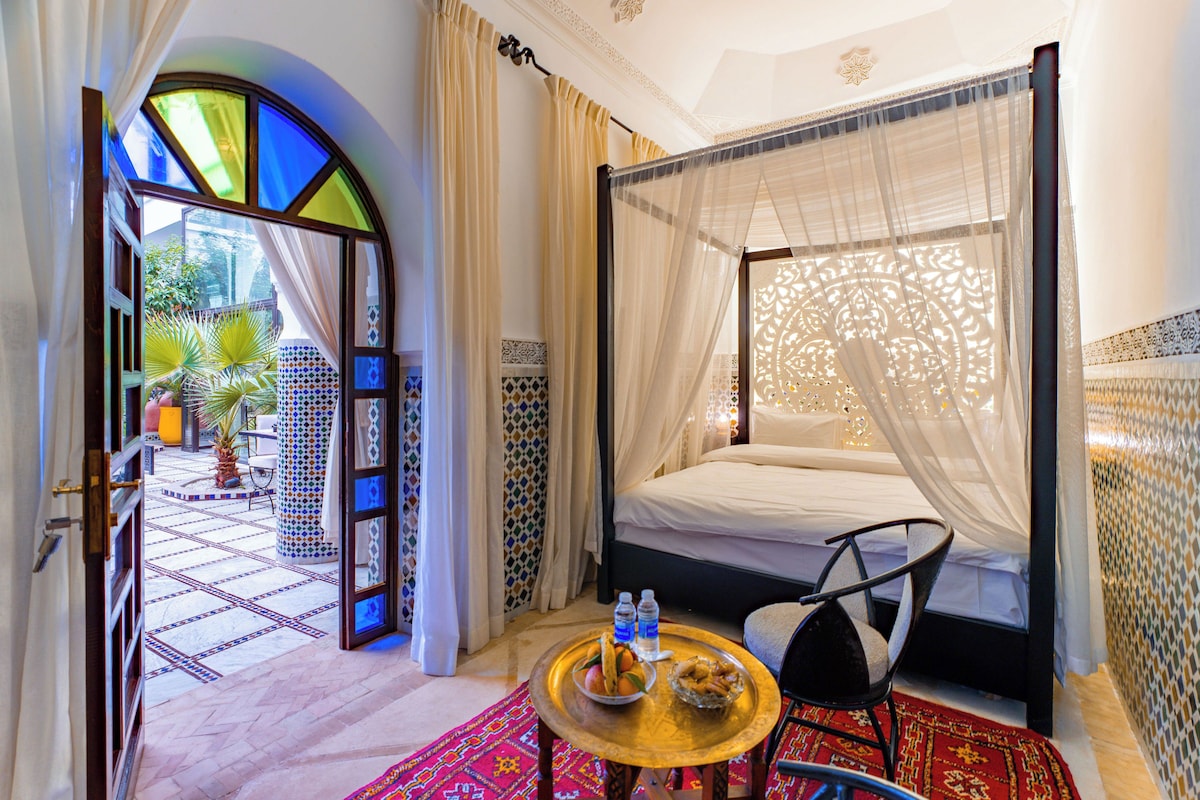 A room with a bed, a table with food, and a view of the outside.