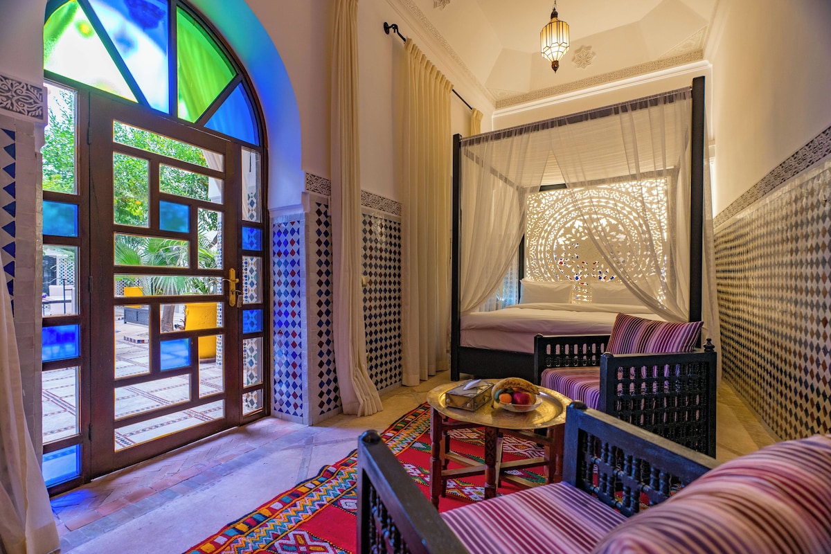 A room with a bed, a window with a view, a table with a basket, and patterned walls.