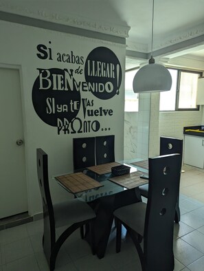 A dining area with a table set for four, chairs, and a wall with a motivational message.