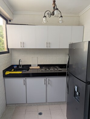 A compact kitchen with white cabinets, a black countertop, a stainless steel refrigerator, and a gas stove. - Apartamento 3 hab. cerca al aeropuerto de Neiva · Ideal familias y grupos (Neiva)