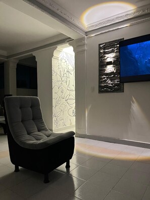 A modern living room with a large TV mounted on the wall, a decorative wall panel, and a plush armchair.