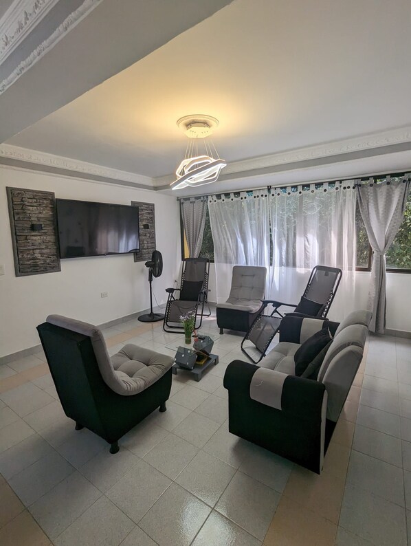 A living room with a sofa set, a flat-screen TV, a fan, and a decorative ceiling light.