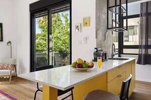 Een moderne keuken met een groot eiland, een zithoek met een bank en uitzicht op groen.