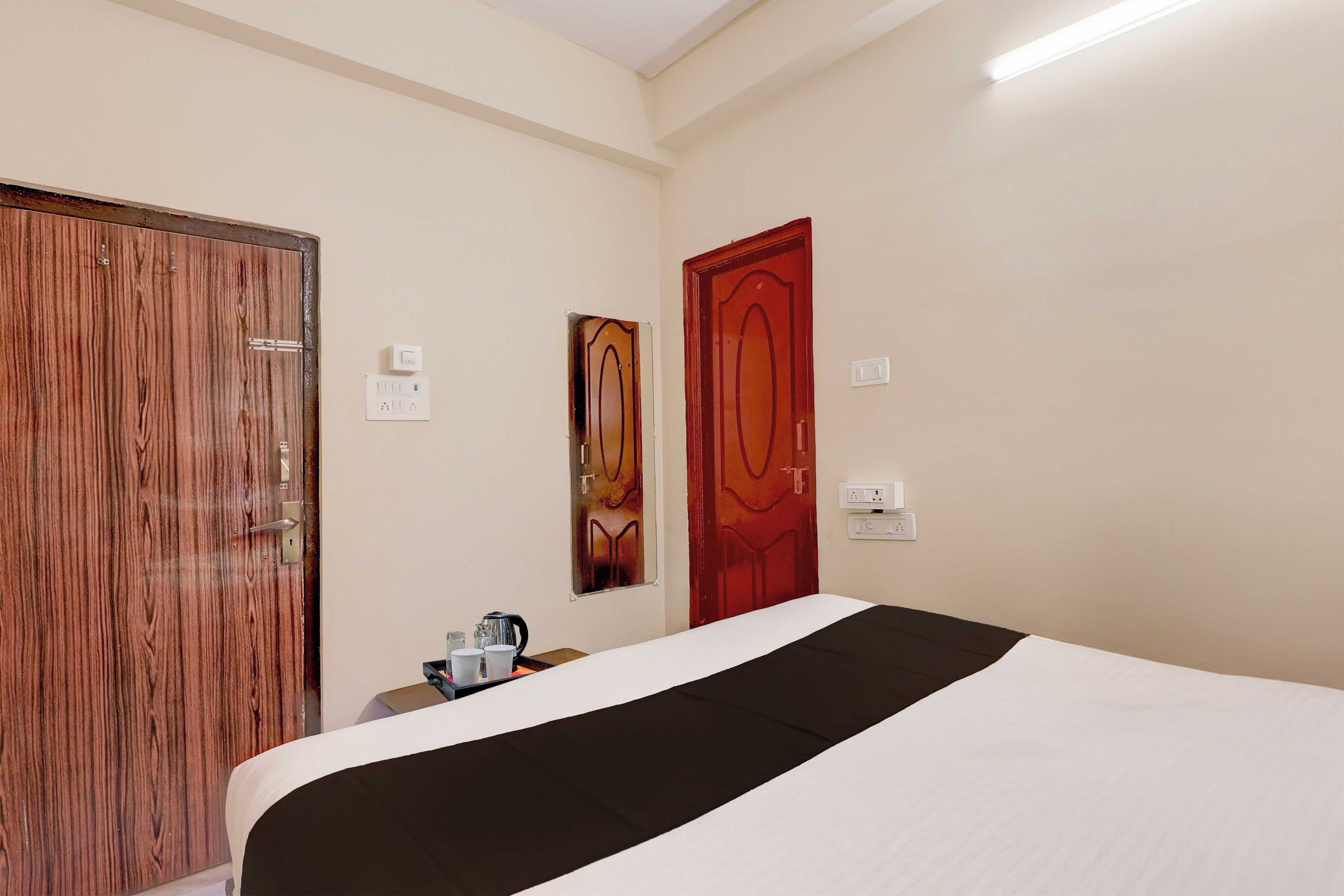 A hotel room with a bed, a wooden wardrobe, a red door, and a painting on the wall.