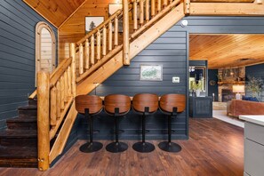 A staircase with wooden railings leading to a dark-paneled room with a bar area featuring four stools. - Smokey Mountain Splendor: Sauna, Pickleball, Game Room & Jacuzzi (Sevierville)