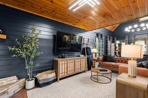 A modern living room with a large flat-screen TV, a wooden cabinet, a sofa, and a coffee table. - Smokey Mountain Splendor: Sauna, Pickleball, Game Room & Jacuzzi (Sevierville)