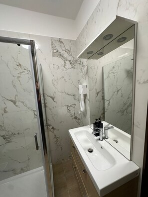 Un baño moderno con cabina de ducha de vidrio, un lavabo blanco con grifo cromado y un espejo grande.