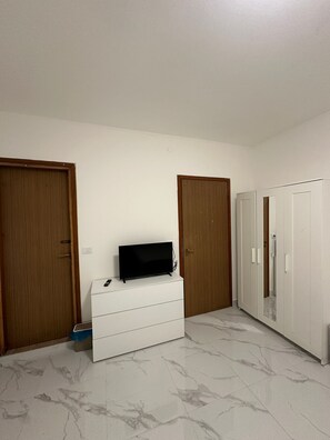Una habitación con un tocador blanco, televisor y armario.