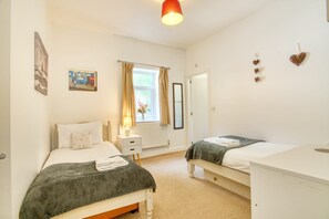 A bedroom with two beds, a bedside table with a lamp, a radiator, and a window with curtains. - Lansdowne Lodge - Pass the Keys (Market Rasen)
