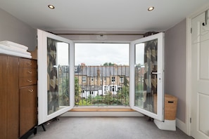 A room with a large sliding glass door leading to a balcony, a wooden wardrobe, and a small woven basket. - Spacious 4 Bed Edwardian London Home with Garden - Pass the Keys (London)