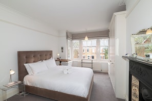 Une chambre à coucher bien aménagée, avec un grand lit, des lampes de chevet, une fenêtre donnant sur des immeubles et une cheminée.