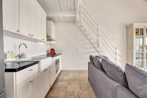 A modern kitchen with white cabinetry, a black countertop, and a red appliance. A grey sofa is positioned near a staircase leading to an upper level. - 2BR Duplex, Marina View, Sleeps 6 · Apt 15 Ocean Breeze (Kralendijk)