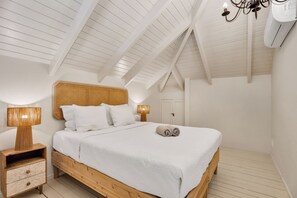 A bedroom with a wooden bed, white bedding, a nightstand with a lamp, and a ceiling fan. - 2BR Duplex, Marina View, Sleeps 6 · Apt 15 Ocean Breeze (Kralendijk)