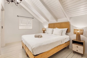 A bedroom with a wooden bed, white bedding, a rattan headboard, two bedside lamps, and a wooden nightstand with drawers. - 2BR Duplex, Marina View, Sleeps 6 · Apt 15 Ocean Breeze (Kralendijk)