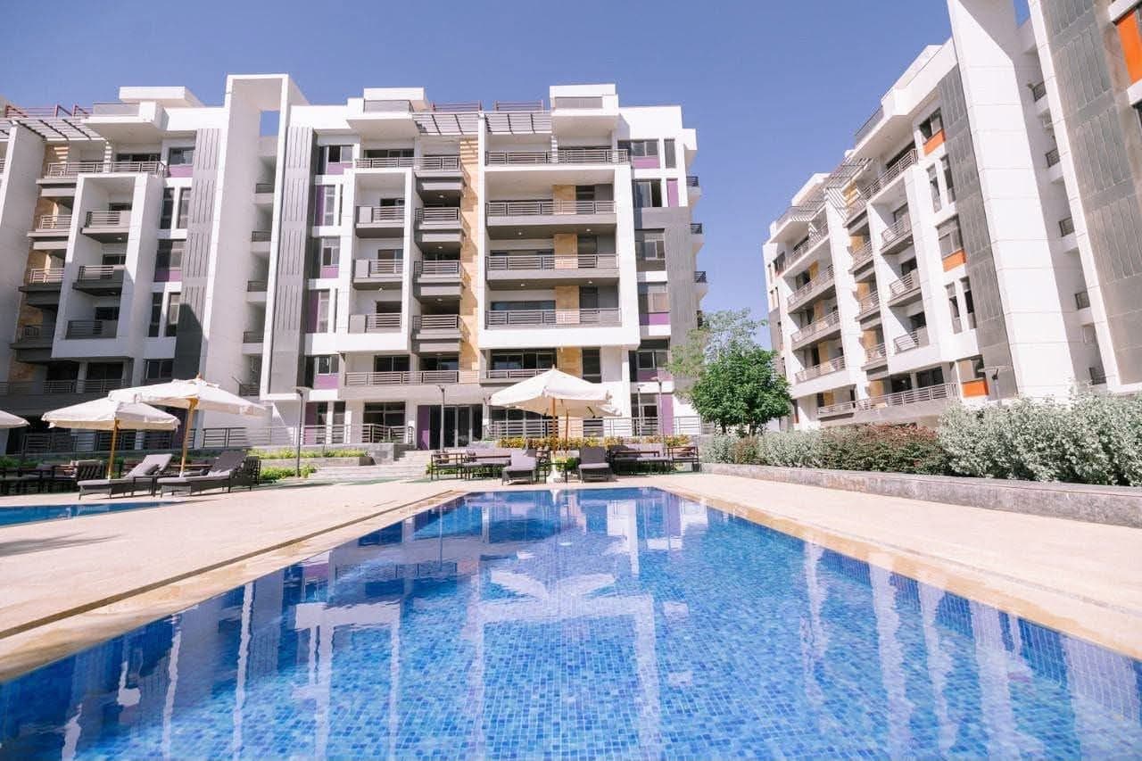 A modern multi-story residential building with balconies, a swimming pool, and outdoor seating.