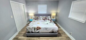 Een slaapkamer met een bed, twee nachtkastjes, een raam met zonwering en een deur.