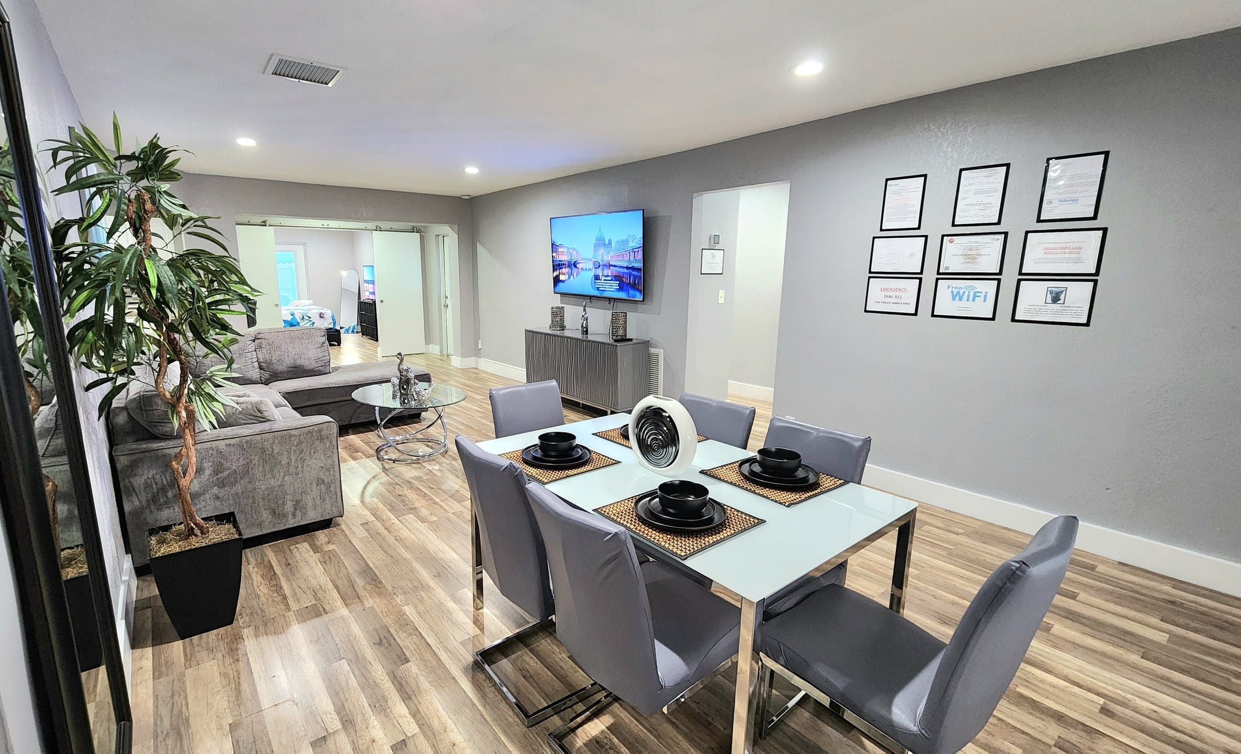 Un salon moderne comprenant un coin repas, un téléviseur à écran plat fixé au mur et plusieurs certificats encadrés accrochés au mur.