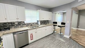 A modern kitchen with white cabinets, a granite countertop, and a dishwasher. - Pool Home w/ 2 Kings near Beach, FLL & Hard Rock (Hollywood)