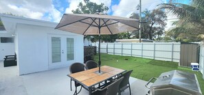 Een terras met een tafel en stoelen, een barbecue en een omheinde tuin.
