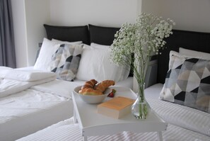 A neatly made bed with white bedding, a bowl of croissants, a book, and a vase with flowers on a bedside table. - New Listing (Davos Platz)