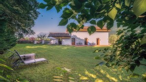 Une maison à l’extérieur blanc et au toit recouvert de tuiles, entourée d’une pelouse bien entretenue et agrémentée de quelques espaces de détente en plein air.