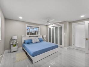 A bedroom with a bed, bedside tables, a ceiling fan, a window, and a wardrobe. - Amazing home in the heart of port charlotte with beautiful water front views (Port Charlotte)