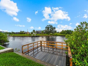 Eine Holzterrasse mit Blick auf einen ruhigen Fluss, umgeben von Grünflächen und einem klaren Himmel.
