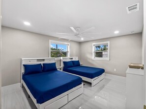 Ein Schlafzimmer mit zwei Betten, einem Deckenventilator und Fenstern.