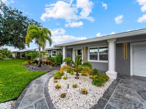 A modern house with a stone pathway leading to the entrance, surrounded by a well-maintained lawn and various plants. - Amazing home in the heart of port charlotte with beautiful water front views (Port Charlotte)