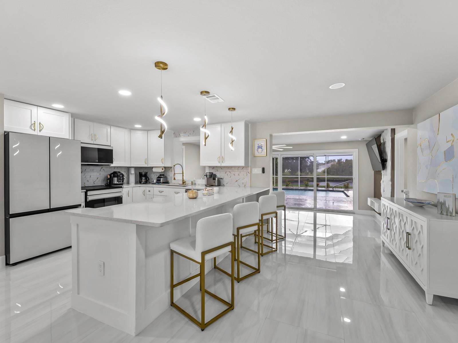 A modern kitchen with white cabinetry, a central island with bar stools, and a view of an outdoor pool.