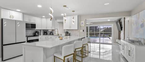 A modern kitchen with white cabinetry, a central island with bar stools, and a view of an outdoor pool.