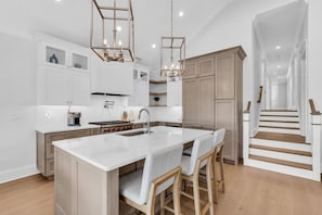 A modern kitchen with a central island, wooden cabinets, and a staircase leading to another level. - Luxury 5BR | Sleeps 16 | 1 Block to Beach & Boardwalk (Ocean City)