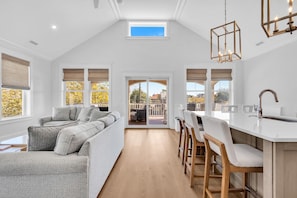 A spacious living area with a sofa, dining table, and chairs, a kitchen with a modern sink, and large windows offering a view of the outdoors. - Luxury 5BR | Sleeps 16 | 1 Block to Beach & Boardwalk (Ocean City)