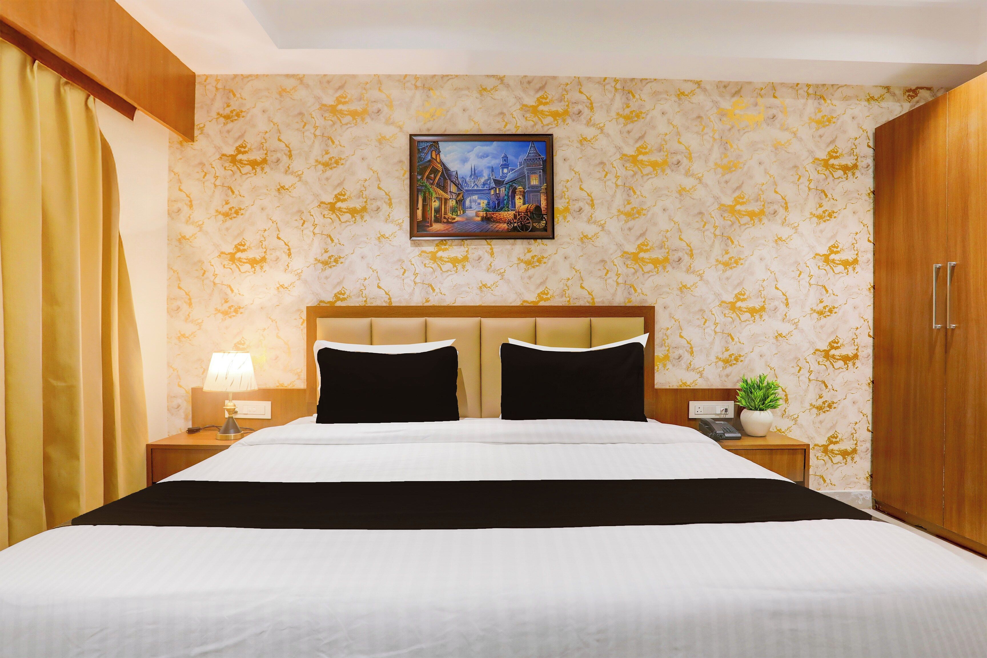Ein Hotelzimmer mit Bett, Nachttisch, Lampe, einem Bild an der Wand und einem Blumentopf.
