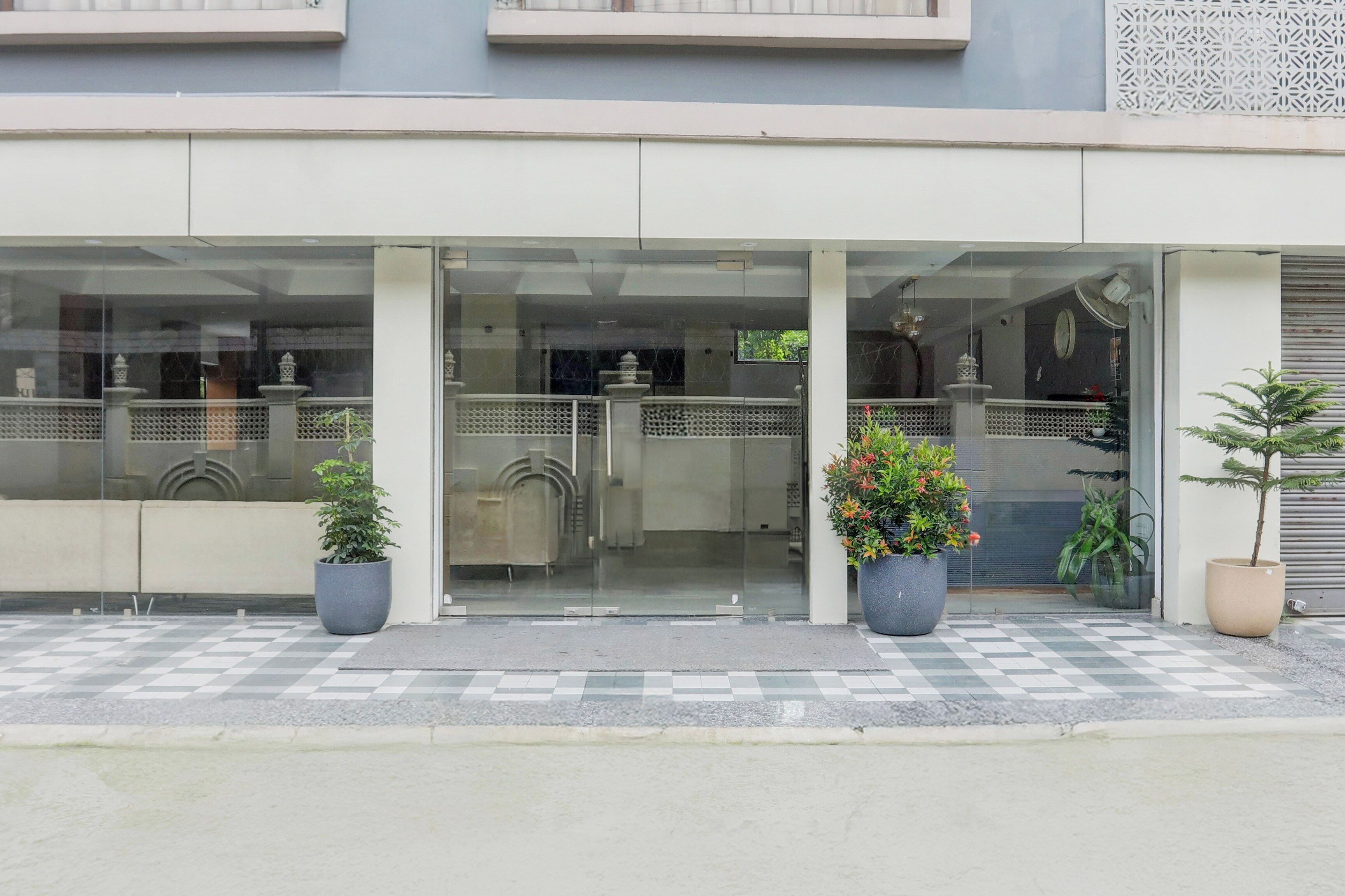 A building entrance with a glass door, potted plants, and a checkered floor.