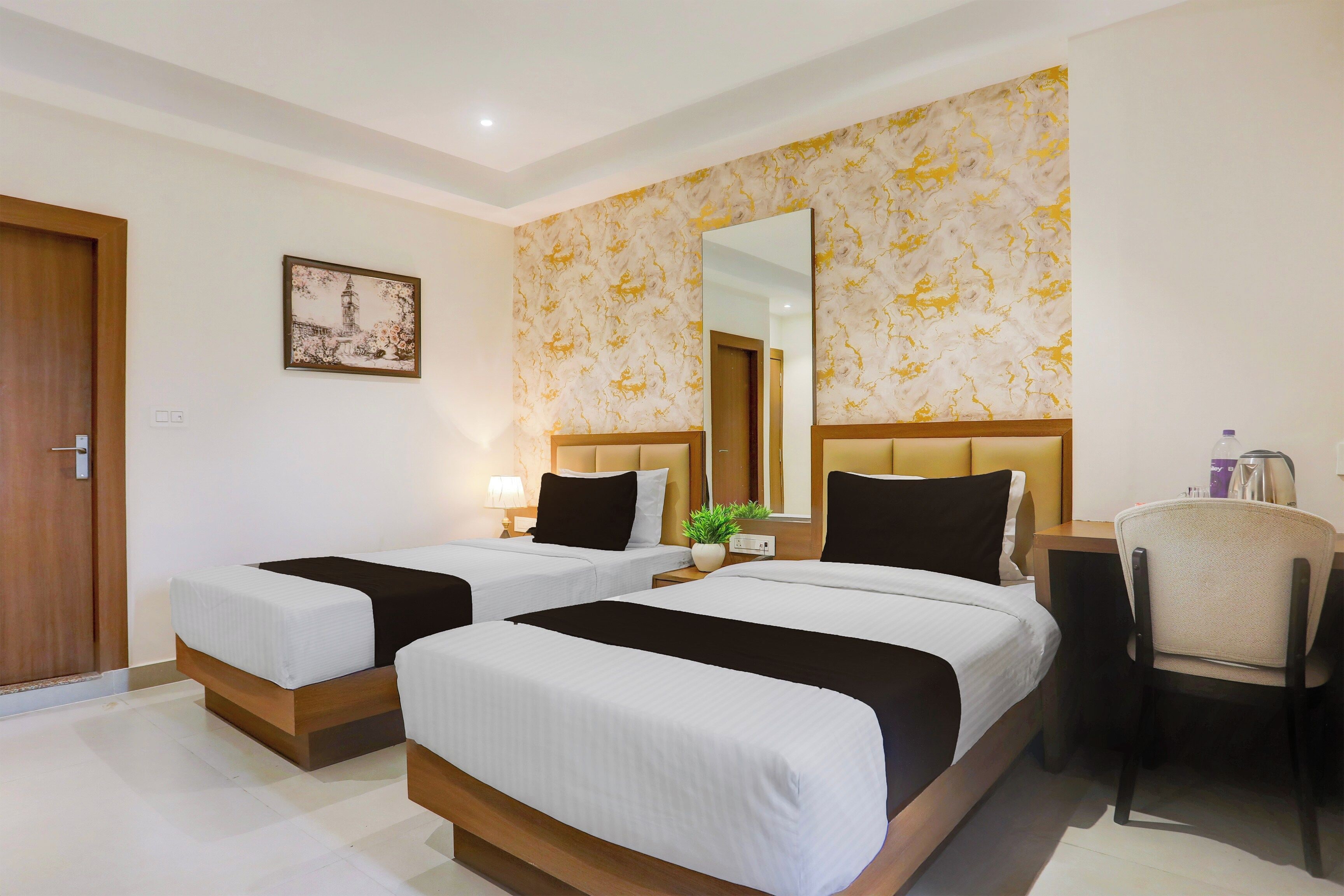 Habitación de hotel con dos camas, una silla, un escritorio, un espejo y un cuadro en la pared.