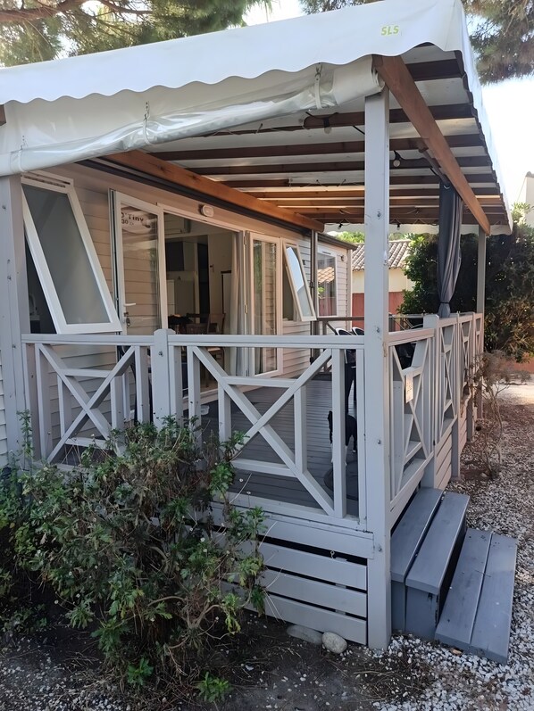 Uma área externa coberta com deck de madeira, corrimão branco e um pequeno alpendre.