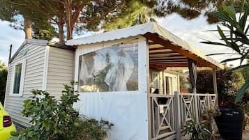 A mobile home with a covered porch, a car parked in front, and various plants around.