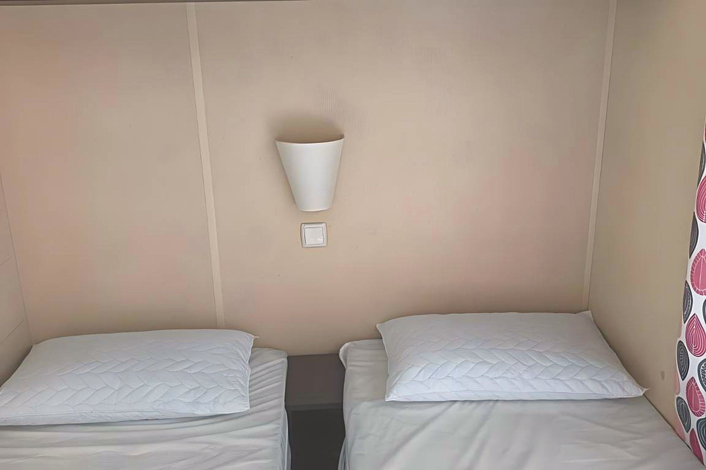 Una camera d'albergo con due letti singoli, una lampada a parete e una piccola finestra.