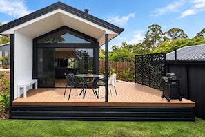 Een modern buitenterras met een eettafel, stoelen, een barbecue en een overdekt zitgedeelte.