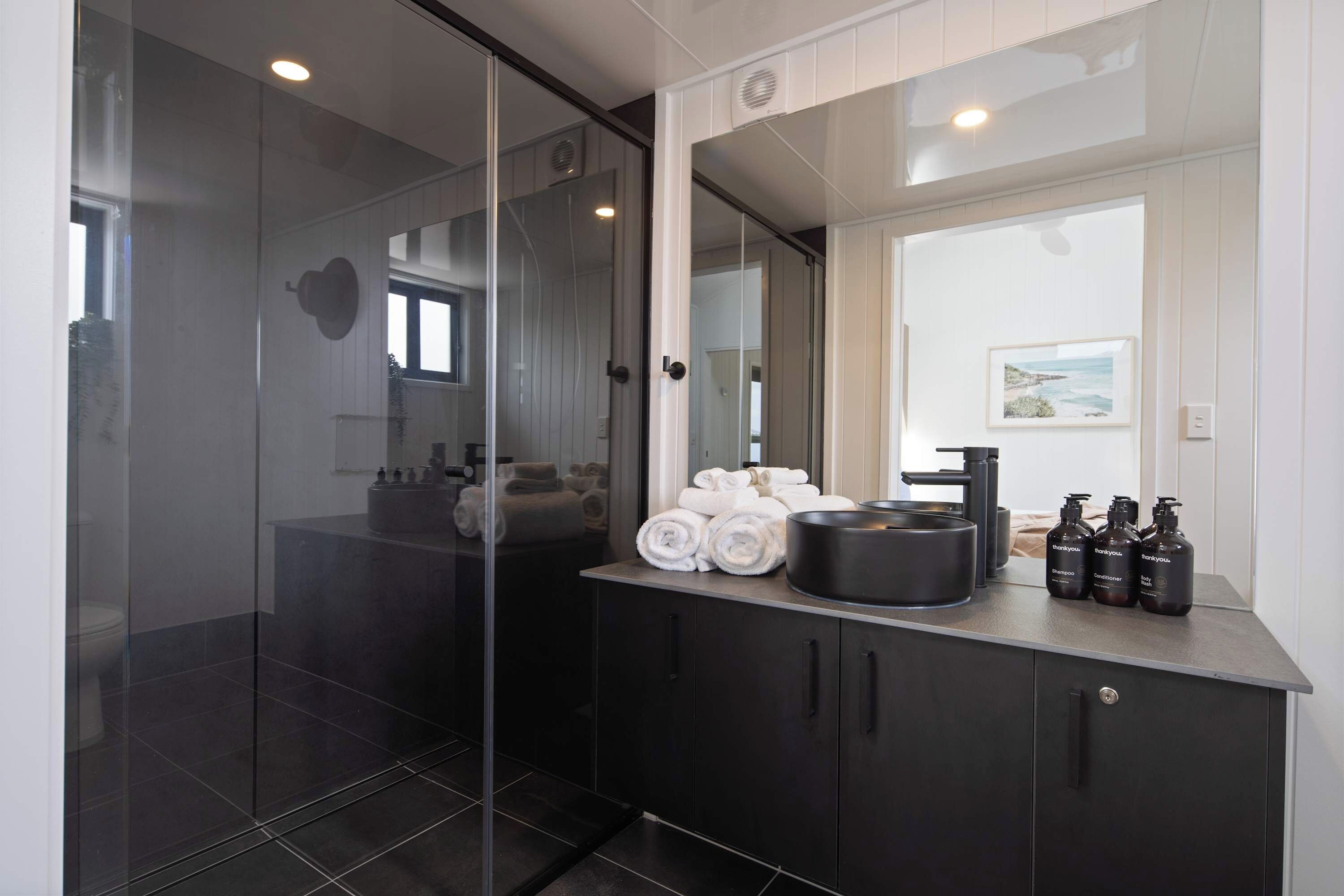 A modern bathroom with a glass shower enclosure, a vanity with a black countertop, and neatly rolled towels.