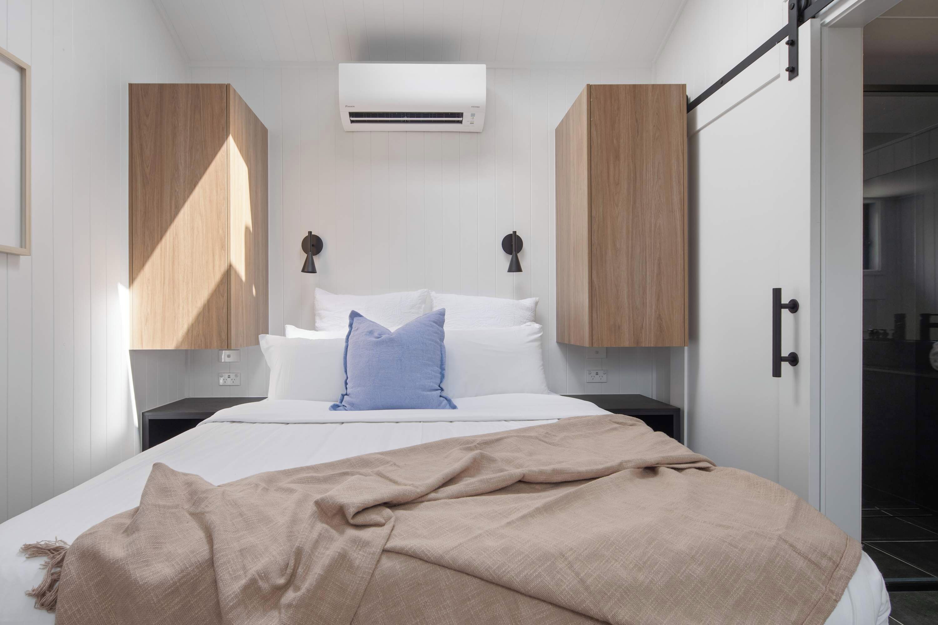A bedroom with a bed, a bedside table, an air conditioning unit, and wooden wardrobes.