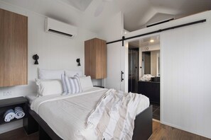 Een moderne slaapkamer met een bed, nachtkastjes, een kledingkast en een badkamer zichtbaar door een geopende deur.