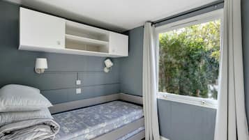 Un dormitorio con cama, mesita de noche, estante en la pared y ventana con cortinas.